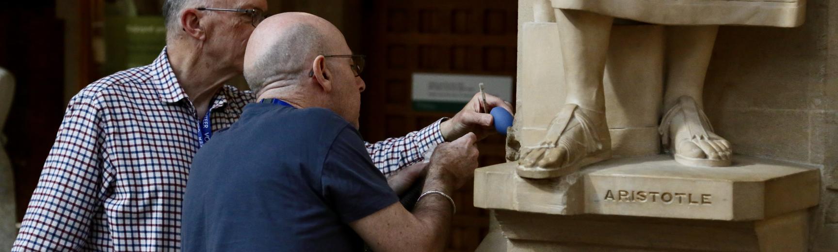 Two male volunteers cleaning the stonework around a statue in the Oxford University Museum of Natural History