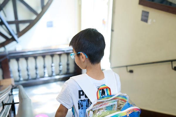 A young boy descends a wooden staircase, wearing a bright backpack on his back. 